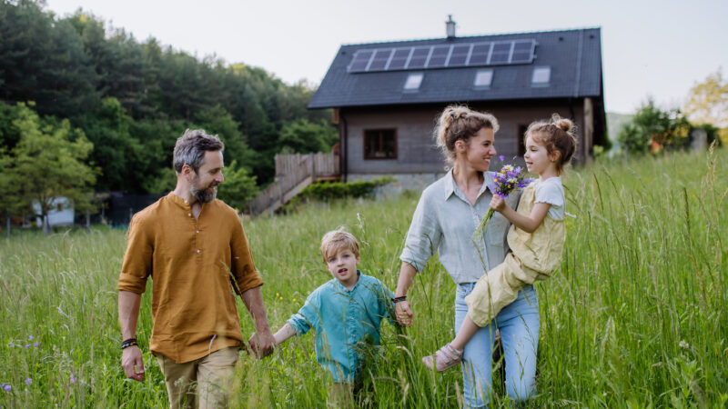 Happy family in front of their house with a solar panels on the roof.