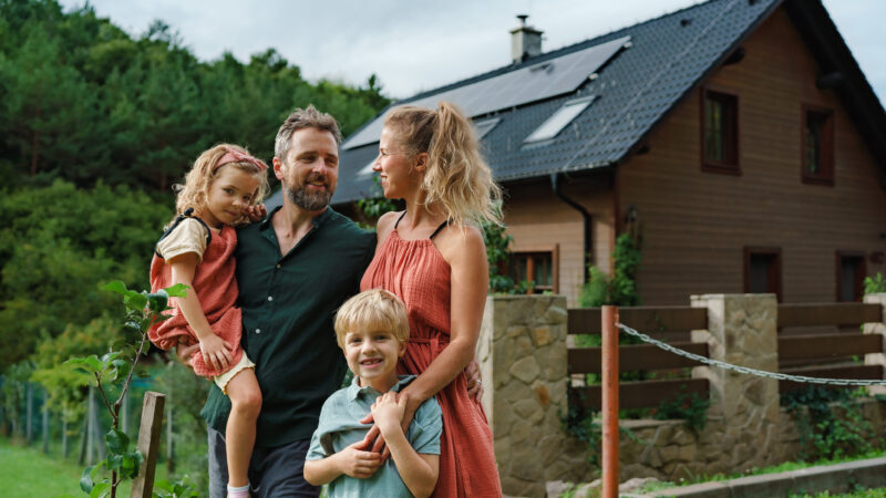 Happy family near their house with a solar panels. Alternative energy, saving resources and sustainable lifestyle concept.